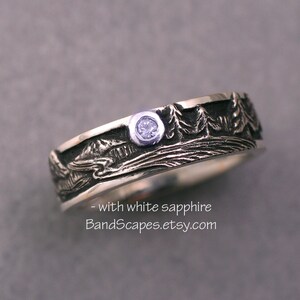 May include: A silver ring featuring a textured landscape relief of trees and mountains with a single bezel-set white sapphire. The ring includes the text - with white sapphire BandScapes.etsy.com printed on the lower portion of the image.