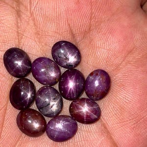 Peut inclure: Un ensemble de neuf rubis étoilés de forme ovale, taillés en cabochon, dans des tons profonds de violet et de rouge. Chaque pierre précieuse présente un effet d'étoile à six branches, appelé astérisme, visible sur les surfaces polies.