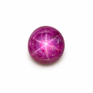 Op de afbeelding: Een ronde, in cabochon geslepen sterrobijn edelsteen met een diepe magenta-roze kleur. De steen vertoont een duidelijk zesstralig stereffect, bekend als asterisme, gecentreerd op het gepolijste oppervlak met zichtbare natuurlijke insluitingen.