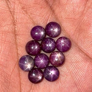 May include: A collection of ten small, round, cabochon-cut star rubies. Each deep magenta-coloured gemstone features a distinct six-rayed star pattern that appears on the polished, domed surface when light reflects off the internal inclusions.