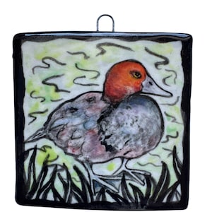 May include: Square ceramic tile featuring a hand-painted duck. The duck has a red head, gray body, and is set against a green and white background with black trim. A metal loop is attached for hanging.