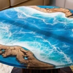 May include: Oval coffee table with a resin top depicting an ocean scene. The table features shades of blue and white resin, with sections of brown wood resembling landmasses. The table is supported by a dark wooden base.
