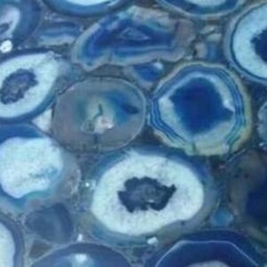 Puede incluir: Una mesa redonda decorativa hecha de rodajas de &aacute;gata azul pulida. La &aacute;gata presenta anillos conc&eacute;ntricos de diferentes tonos de azul y blanco, creando un patr&oacute;n natural &uacute;nico. La superficie es lisa y brillante, con un aspecto de mosaico. Di&aacute;metro aproximado de 60 cm.