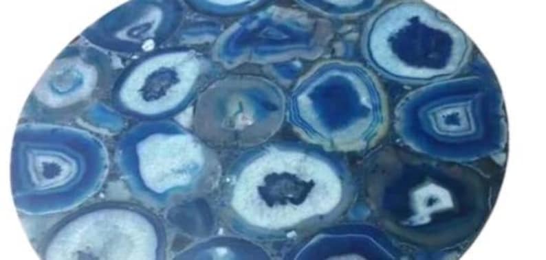 Puede incluir: Una mesa redonda decorativa hecha de rodajas de &aacute;gata azul pulida. La &aacute;gata presenta anillos conc&eacute;ntricos de diferentes tonos de azul y blanco, creando un patr&oacute;n natural &uacute;nico. La superficie es lisa y brillante, con un aspecto de mosaico. Di&aacute;metro aproximado de 60 cm.