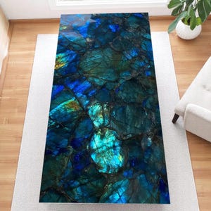 Puede incluir: Una mesa de centro rectangular con una llamativa superficie iridiscente. La parte superior de la mesa presenta un mosaico de azules profundos, verdes y toques de oro, que se asemeja a una piedra preciosa pulida. La mesa está sobre una alfombra clara.