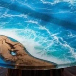 May include: Round table with a resin ocean design. The table features a vibrant blue and white wave pattern, with a section of brown, textured land. The table's design evokes a coastal theme.