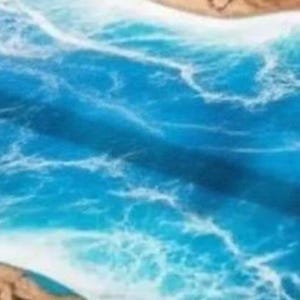 May include: A handcrafted epoxy resin table with a vibrant ocean design. The table features shades of blue and white, mimicking waves and sea foam. The edges are a natural wood color, creating a coastal theme. The table's surface is smooth and glossy.