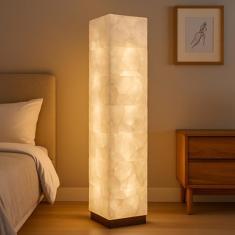 May include: A tall, rectangular floor lamp with a textured, off-white shade. The lamp is composed of stacked, illuminated sections, and sits on a dark brown base. The lamp is a decorative lighting fixture.