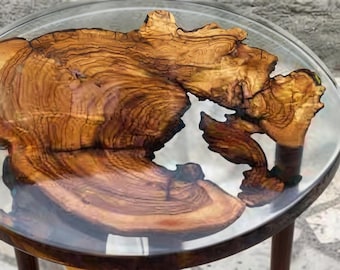 May include: A round side table featuring a natural, irregular olive wood slab embedded within a clear, circular resin tabletop. The wood displays prominent, swirling grain patterns in shades of golden brown and amber, supported by wooden legs.