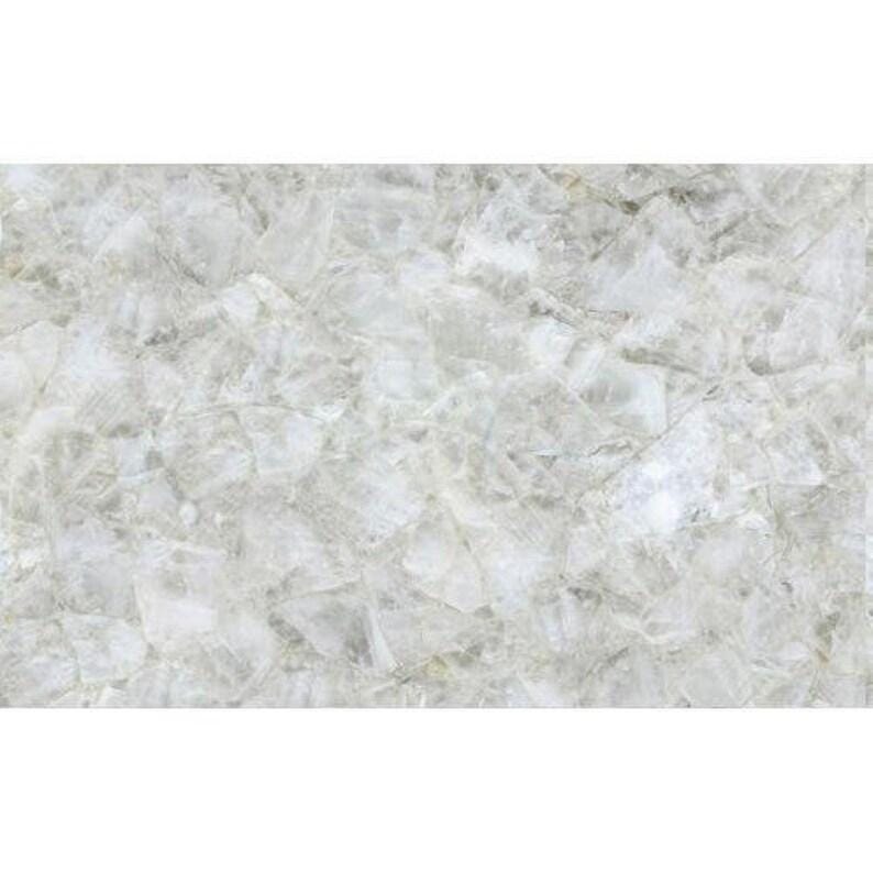 May include: A close-up of a white and gray stone surface with a crystalline appearance. The surface is composed of irregular, interlocking shapes, creating a textured, mosaic-like pattern. The overall effect is a cool, neutral aesthetic.