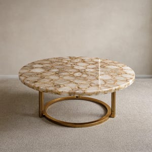 May include: A round coffee table featuring a polished tabletop composed of numerous beige and cream-colored agate slices with a smooth, glossy finish. The table is supported by a circular gold-toned metal base with three vertical legs.