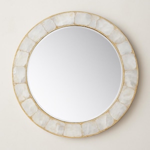 May include: Circular mirror featuring a gold-toned metal frame and a border of white, irregularly shaped tiles. The reflective surface is smooth and circular. A decorative wall mirror, suitable for various interior styles.