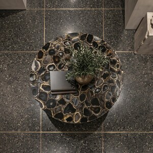May include: A circular coffee table featuring a mosaic surface of dark, polished agate slices with natural banding. A small potted green plant and a stack of two dark-colored books are placed on the center of the table, viewed from directly above.