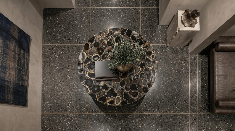 May include: A circular coffee table featuring a mosaic surface of dark, polished agate slices with natural banding. A small potted green plant and a stack of two dark-colored books are placed on the center of the table, viewed from directly above.