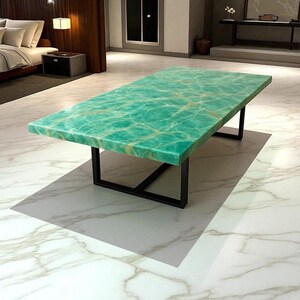 May include: A rectangular coffee table with a green and gold marbled top. The table has a black metal base. The table is in a room with marble flooring and a bed in the background.