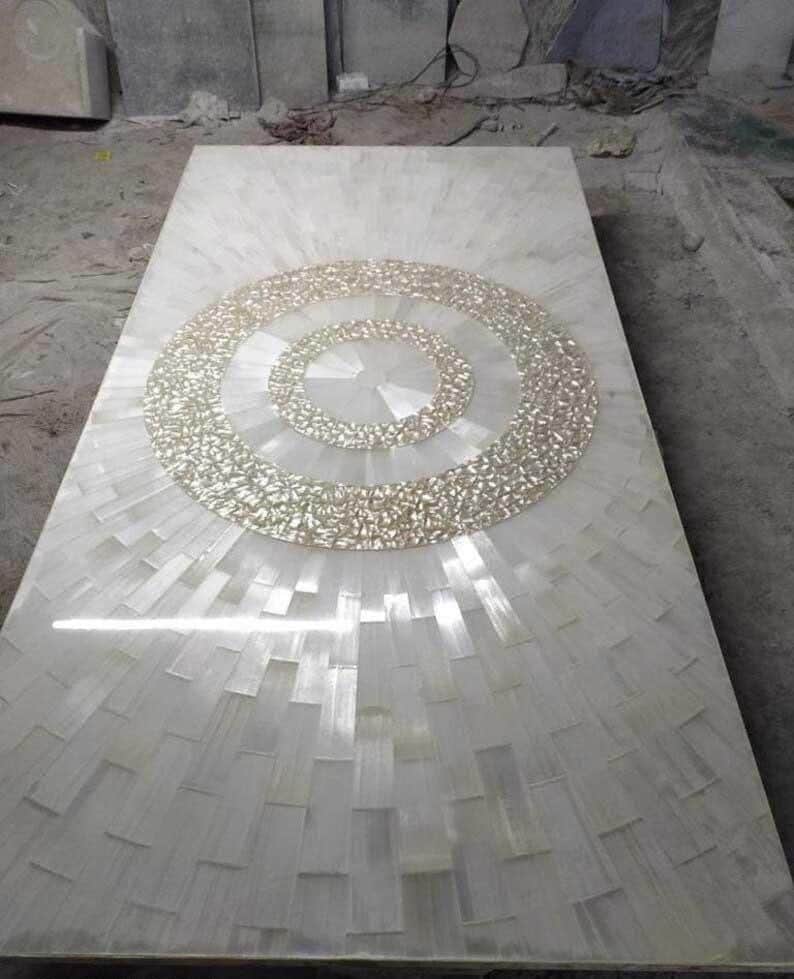 Puede incluir: Una mesa rectangular de piedra blanca con un dise&ntilde;o circular texturizado en el centro. El dise&ntilde;o est&aacute; hecho de peque&ntilde;as piezas de color claro, y la superficie de la mesa tiene un patr&oacute;n radiante.