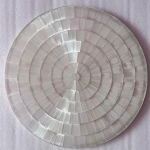 Op de afbeelding: Een ronde, transparante decoratieve plaat met een concentrisch ontwerp. De plaat is gemaakt van een doorschijnend materiaal, mogelijk glas of kristal, en heeft een reeks cirkelvormige segmenten die vanuit het midden uitstralen.