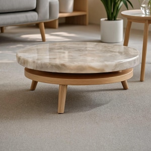 May include: A low, round coffee table featuring a polished, beige and grey marbled stone top. The tabletop rests on a circular wooden frame supported by four short, tapered wooden legs, creating a stable and elevated surface for living spaces.