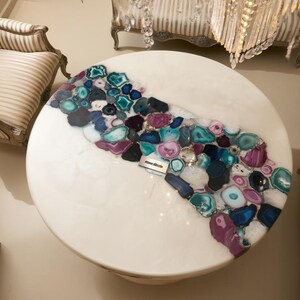 May include: A round white coffee table with a decorative inlay of colorful agate stones in shades of blue, purple, and teal. The table is surrounded by striped upholstered furniture, creating a luxurious living room setting.