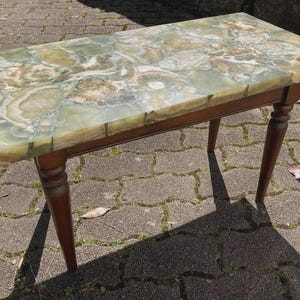 May include: A rectangular coffee table with a green and brown patterned stone top. The table has a dark brown wooden frame and four turned legs. The table is approximately 36 inches long and 18 inches wide.