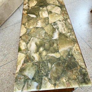 K&ouml;nnte beinhalten: Rechteckiger Couchtisch mit einer Mosaikplatte aus unregelm&auml;&szlig;ig geformten gr&uuml;nen und wei&szlig;en Steinen. Der Tisch hat einen Holzrahmen und Beine, und die Steine sind in einem zuf&auml;lligen Muster angeordnet.