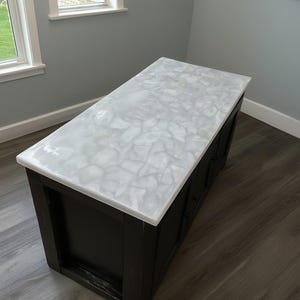 Puede incluir: Una taza de cerámica blanca con un asa negra y el texto "But First, Coffee" en negro, con una fuente de estilo manuscrito. La taza está sobre una superficie blanca.