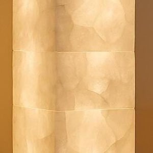 May include: A tall, rectangular floor lamp with a warm, glowing light. The lamp is made of a light-colored, textured material, possibly alabaster or a similar stone. The base is a dark brown color.