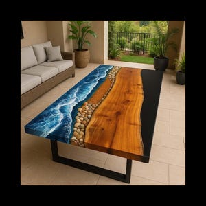 Op de afbeelding: Een rechthoekige salontafel met een uniek ontwerp. De tafel heeft een houten oppervlak met een gedeelte dat een strandscène nabootst met blauwe golven, zand en kiezels. De tafel heeft een zwart metalen onderstel.