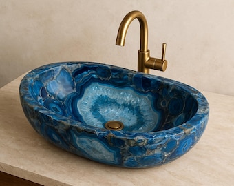 May include: An oval-shaped, blue agate stone sink with a gold faucet. The sink's interior features a lighter blue pattern, and the faucet has a curved spout and a single handle. The sink is set on a light-colored countertop.