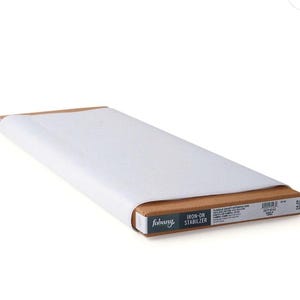 May include: A roll of white fabric wrapped in paper, resting on a brown cardboard box. The box has the brand name "fabany" and the text "IRON-ON STABILIZER". The product is for fusible craft interfacing.