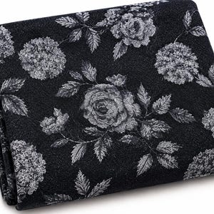 May include: A folded piece of black fabric featuring a repeating white floral pattern of roses and hydrangeas. The textile has a textured appearance with detailed botanical illustrations of flowers and leaves printed across the dark surface.