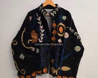 May include: Black jacket with colorful floral embroidery. The jacket features a collar and is adorned with orange, blue, pink, and gold thread. The text "Sanatextile Creations" is visible on the jacket.