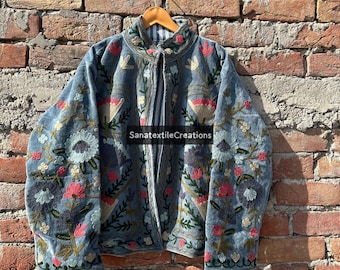 Puede incluir: Una chaqueta azul bordada con diseños florales en rosa, blanco y verde. La chaqueta tiene mangas largas y cuello alto. El texto "SanatextileCreations" es visible en la chaqueta.