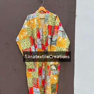 May include: A colorful patchwork kimono robe with a variety of patterns and colors, including orange, green, yellow, and red. The robe is hanging on a wooden hanger. The text "SanatextileCreations" is visible on the front of the robe.