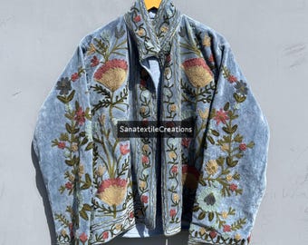 May include: A light blue velvet jacket with intricate floral embroidery in shades of pink, gold, and green. The jacket features a high collar and is embellished with the text "SanatextileCreations".