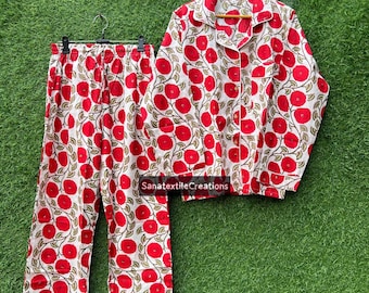 May include: A two-piece pajama set featuring a white background with a repeating pattern of large red flowers and green leaves. The set includes a button-down shirt and matching pants. The shirt is on a wooden hanger.