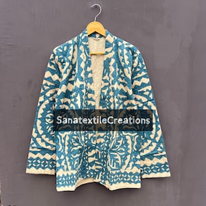 May include: A blue and cream-colored patterned jacket with a quilted design. The jacket is hanging on a wooden hanger. The text "SanatextileCreations" is visible on the front of the jacket.