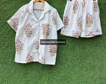 May include: White pajama set with a floral print in pink and green. The set includes a short-sleeved button-down shirt and matching shorts. The shirt has a pocket and green trim. The shorts have a drawstring waist. The text "SanatextileCreations" is visible.