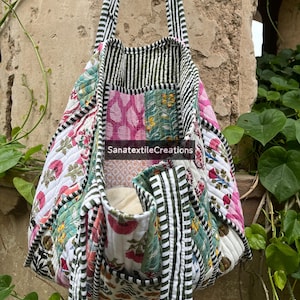 Pode incluir: Bolsa tote acolchoada com um design de patchwork com estampas florais e listradas em branco, rosa, verde e preto. A bolsa tem dois bolsos e alças longas listradas em preto e branco. O texto "SanatextileCreations" é visível.