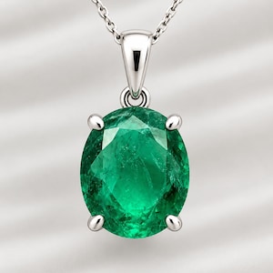 Può includere: Una collana con pendente caratterizzata da una grande pietra preziosa verde dal taglio ovale, incastonata in una montatura in metallo argentato a quattro griffe. Il pendente è sospeso a una sottile catenina argentata con una contromaglia lucida.