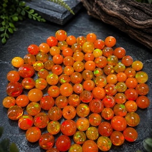 May include: A collection of round, translucent orange beads with iridescent flashes of green and yellow. The beads vary slightly in size and display a polished, glossy finish, creating a vibrant, warm-toned cluster of spherical gemstone components.