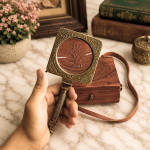 May include: A square brass magnifying glass with a textured handle, featuring the engraved text "HENRY HUGHES SON LTD. LONDON" and "1941" around the circular lens. The frame has decorative corner details and a hinged connection to the handle.