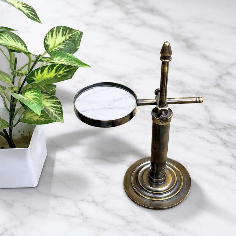 Pu&ograve; includere: Una lente d'ingrandimento in ottone in stile vintage con lente rotonda e interno marmorizzato. La lente &egrave; montata su un supporto verticale con base circolare. Il design evoca un'estetica classica e antica, adatta all'esposizione o all'uso.