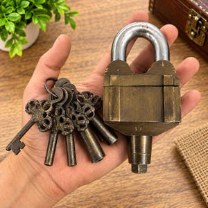 May include: A heavy brass padlock with a silver-toned steel shackle and the number 17 engraved on the front, accompanied by a ring of five matching antique-style brass keys with ornate, decorative bows and cylindrical shafts.