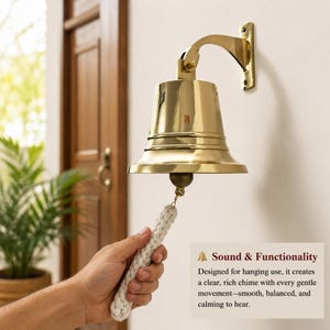 Pode incluir: Uma campainha de parede em lat&atilde;o polido com um suporte de montagem curvo e uma corda tran&ccedil;ada branca grossa. A campainha tem uma superf&iacute;cie lisa e reflexiva com um badalo preso no interior. O texto na imagem diz Sound & Functionality.