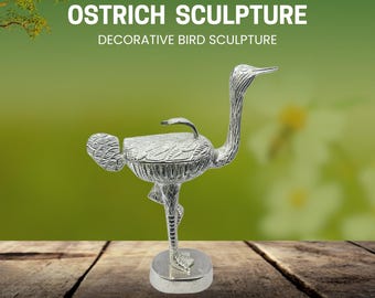 Op de afbeelding: Zilveren struisvogels beeldhouwwerk met de tekst "OSTRICH SCULPTURE" en "DECORATIVE BIRD SCULPTURE". Het beeldhouwwerk staat op een houten oppervlak met een groene achtergrond. De struisvogel staat op één been.