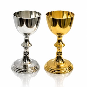 Könnte beinhalten: Zwei Kelche, einer silberfarben und einer goldfarben, werden vor einem weißen Hintergrund gezeigt. Der silberne Kelch hat einen gewellten Rand und einen detaillierten Stiel. Der goldene Kelch hat eine glatte, reflektierende Oberfläche. Beide haben einen runden Fuß.