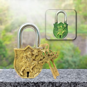 Könnte beinhalten: Ein dekoratives Messing-Vorhängeschloss mit einem silbernen Bügel und zwei Schlüsseln. Das Vorhängeschloss hat ein geprägtes Design einer Gottheit. Eine kleinere, grüne Version des Vorhängeschlosses ist oben rechts abgebildet. Die Schlüssel und das Vorhängeschloss haben eine antike Goldoberfläche.