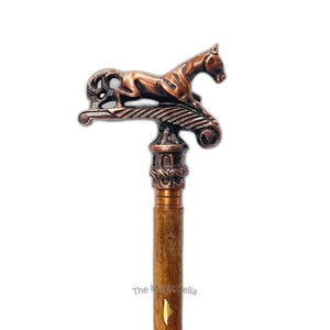 May include: A decorative walking stick featuring a bronze-coloured horse figure on the handle. The handle is light brown with a wood grain texture. The stick has a decorative bronze-coloured column design between the handle and the shaft.