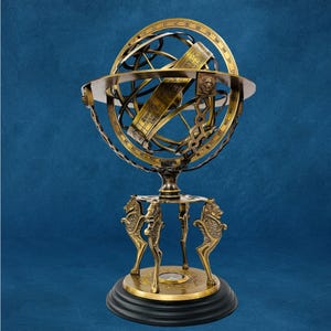 May include: A detailed brass armillary sphere on a black base. The sphere features intricate rings and a central band with text. The base is supported by four lion-shaped legs. The overall design is antique and decorative.